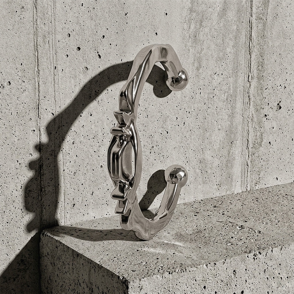 Heavy sculptural cuff with ridged crown and faceted terminals standing upright against concrete wall, A Gross Domestic Product