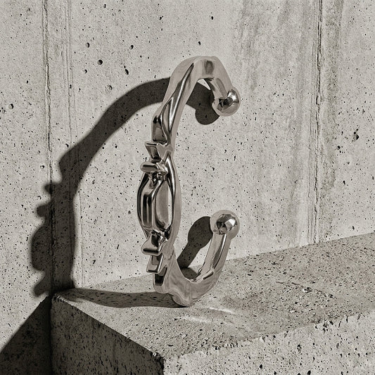 Heavy sculptural cuff with ridged crown and faceted terminals standing upright against concrete wall, A Gross Domestic Product