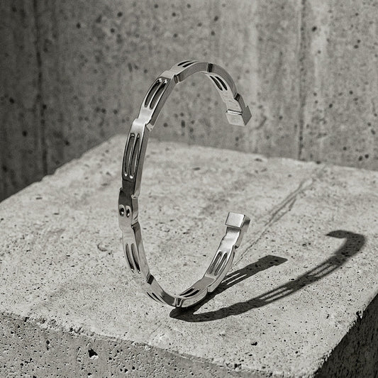 Slim sculptural cuff with pierced oval reliefs and stepped upper edge upright on concrete pedestal, A Gross Domestic Product