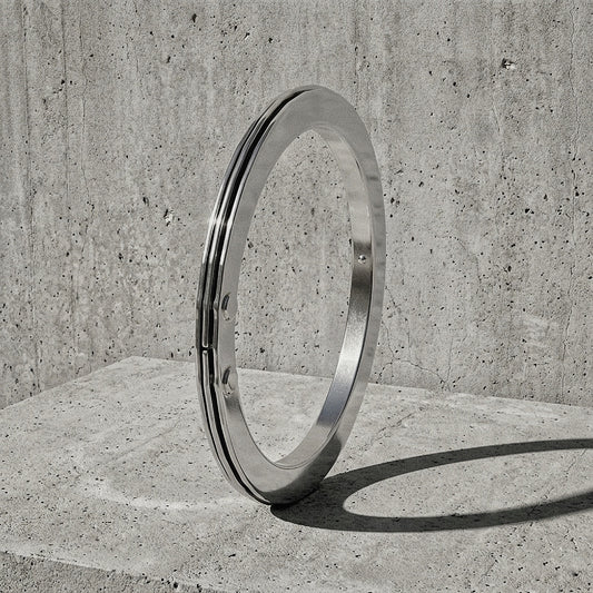 Junction Bangle in sterling silver — three-band rigid bracelet standing on concrete, side profile showing riveted structural node, A Gross Domestic Product