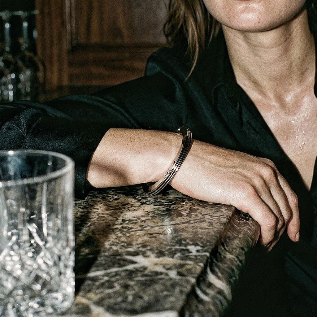 Sterling silver three-band bangle on wrist, dark silk shirt, marble bar, editorial low light