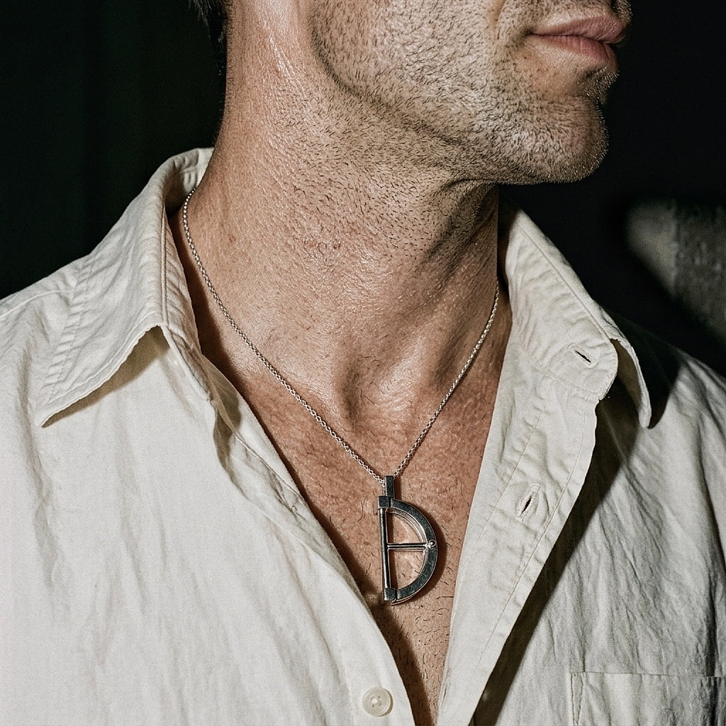 Sterling silver architectural pendant on male chest with open white shirt, editorial low light