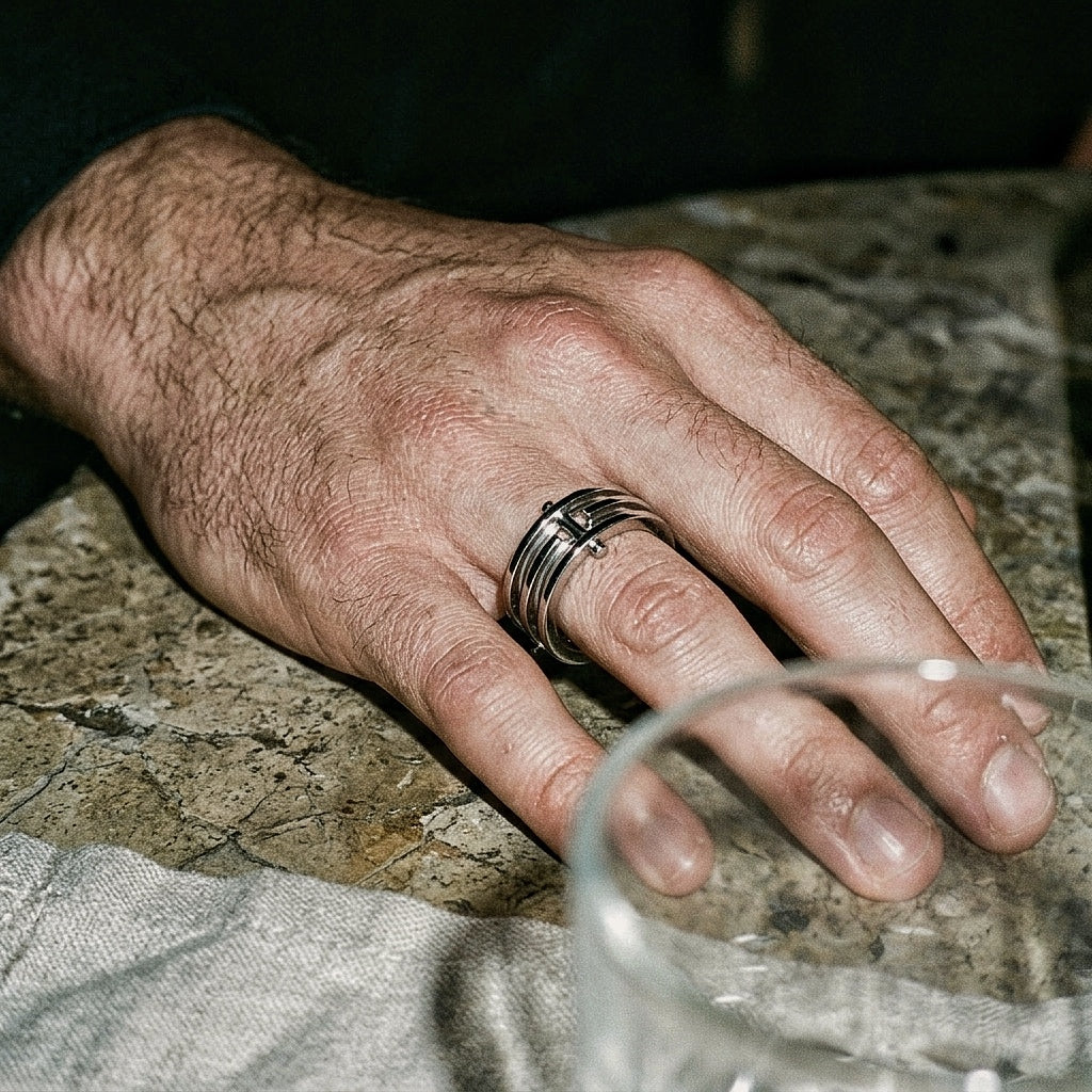 Three-band sterling silver ring on male hand resting on marble surface, editorial low light