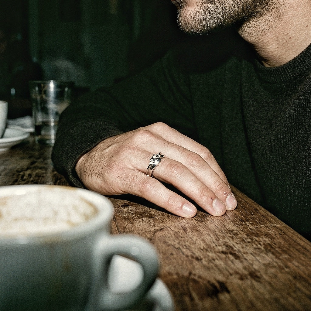 Sterling silver textured ring on male hand resting on wooden bar with coffee cup, editorial warm light