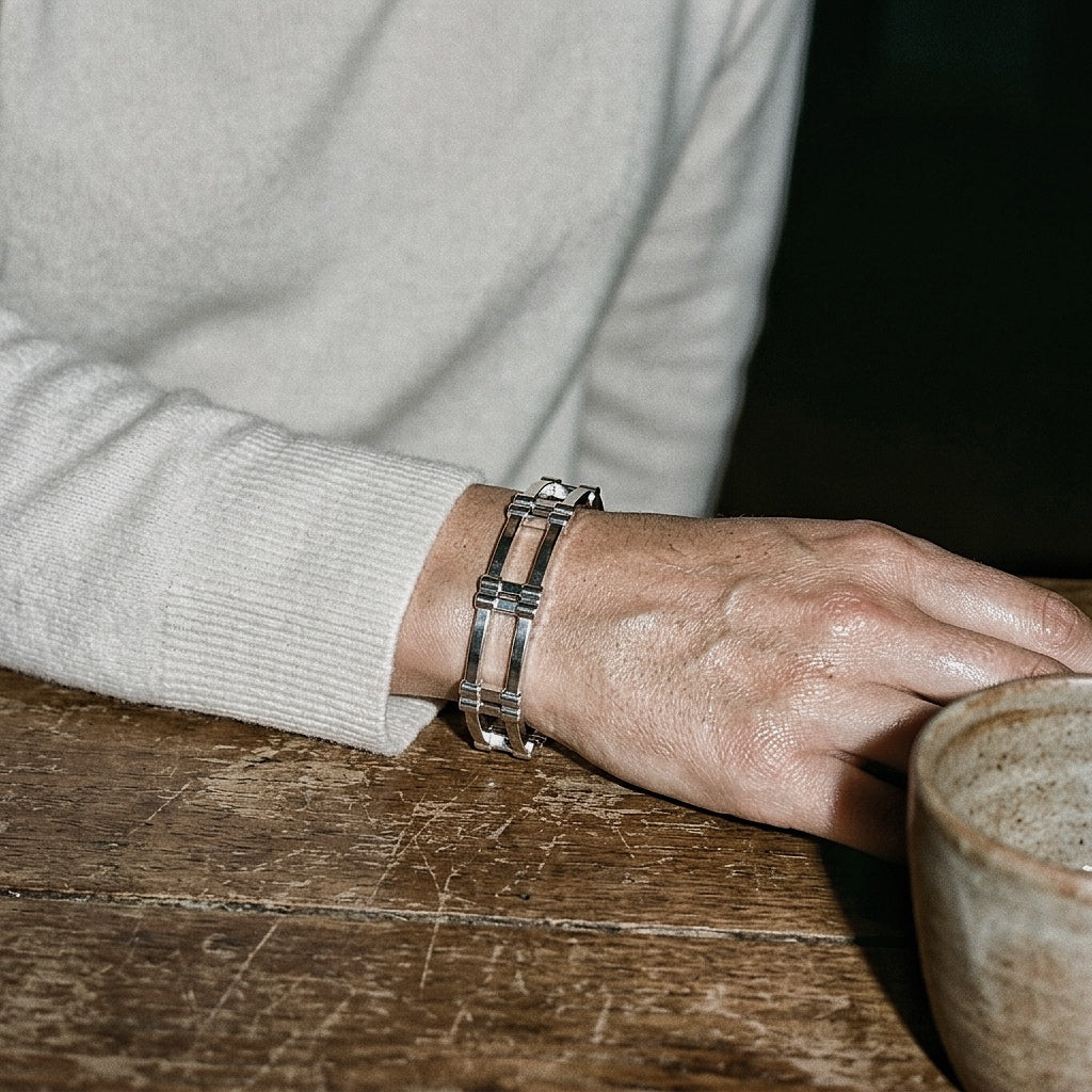 Architectural sterling silver cuff on forearm in cream cashmere sweater with ceramic vessel on weathered wood table